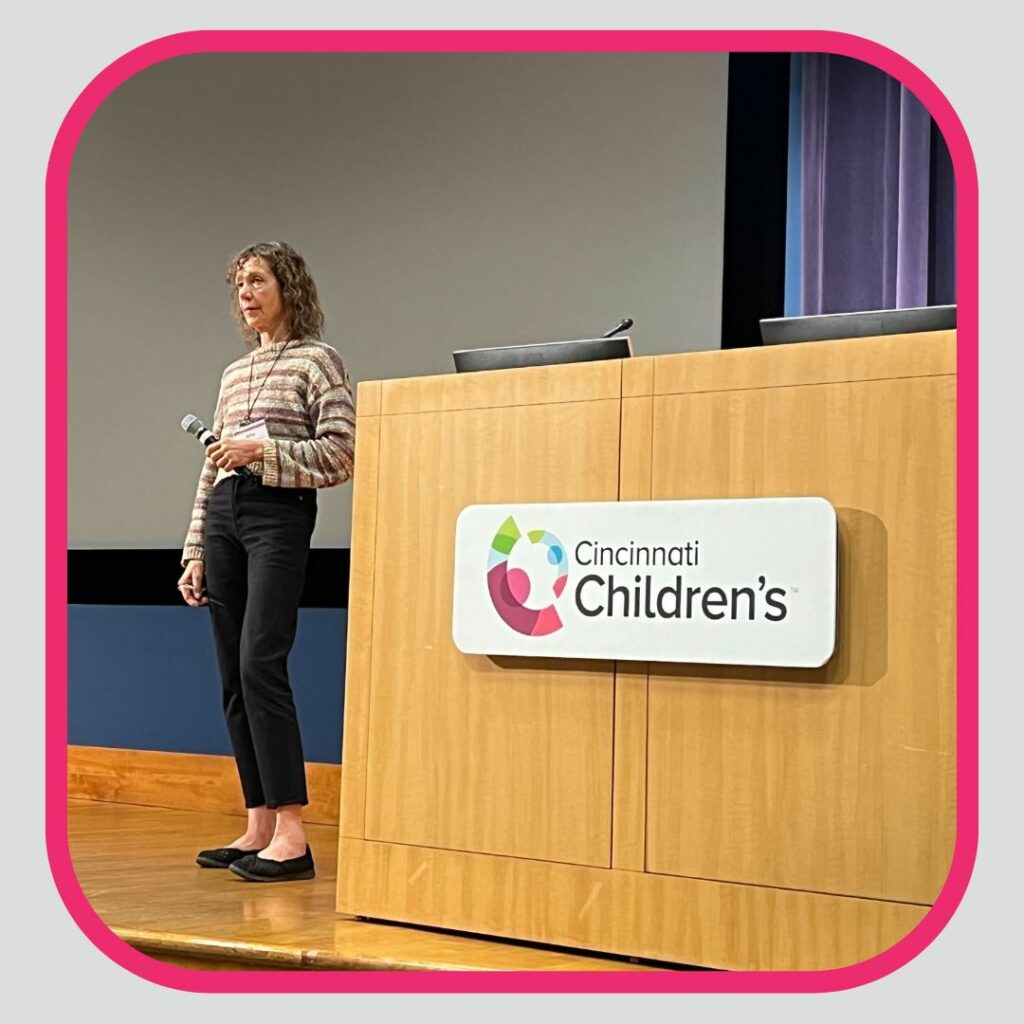 woman holding a microphone standing next to a podium with a cincinnati Children's hospital logo on it