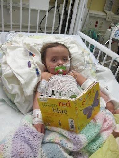 a toodler laying in a hospital bed reading a children's book